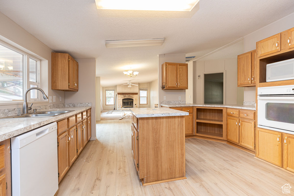 Kitchen with white appliances, light wood-type flooring, a kitchen island, light countertops, and open floor plan