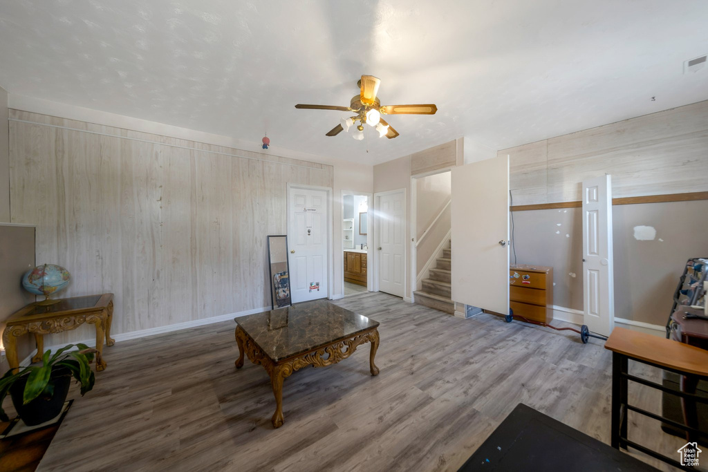 Living room featuring a ceiling fan, wood finished floors, stairway, and wooden walls