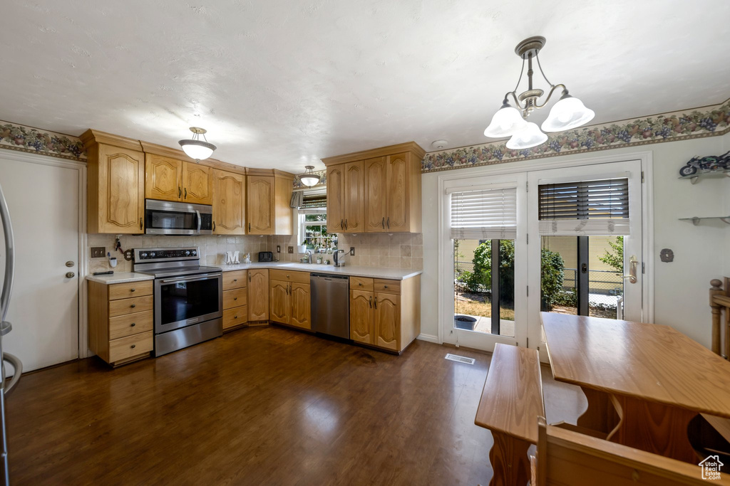 Kitchen with appliances with stainless steel finishes, light countertops, a chandelier, and tasteful backsplash