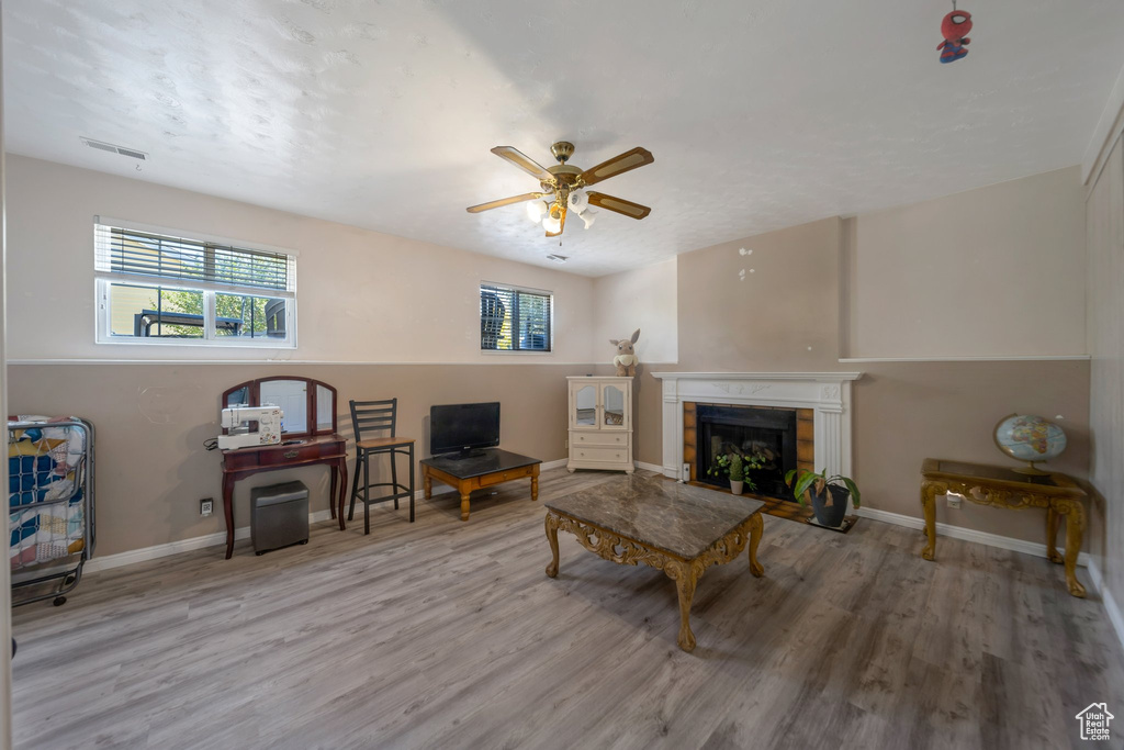Living room featuring plenty of natural light, wood finished floors, a premium fireplace, and a ceiling fan