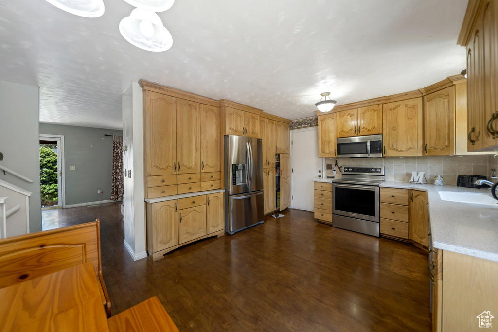 Kitchen with appliances with stainless steel finishes, light countertops, dark wood finished floors, and backsplash