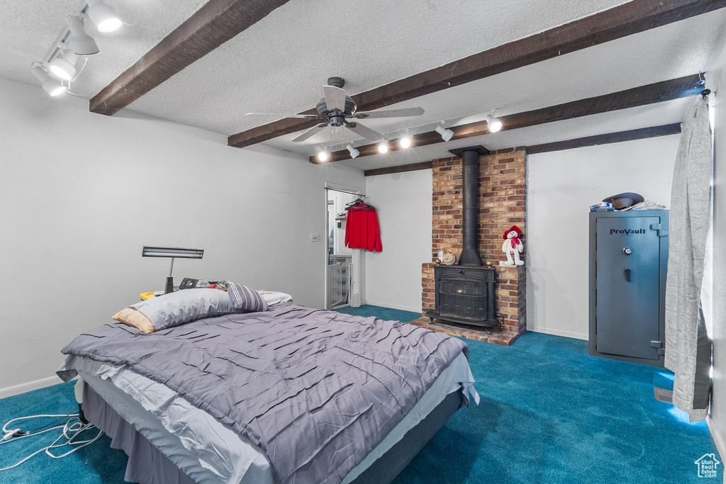 Bedroom with carpet flooring, a textured ceiling, track lighting, beamed ceiling, and a wood stove