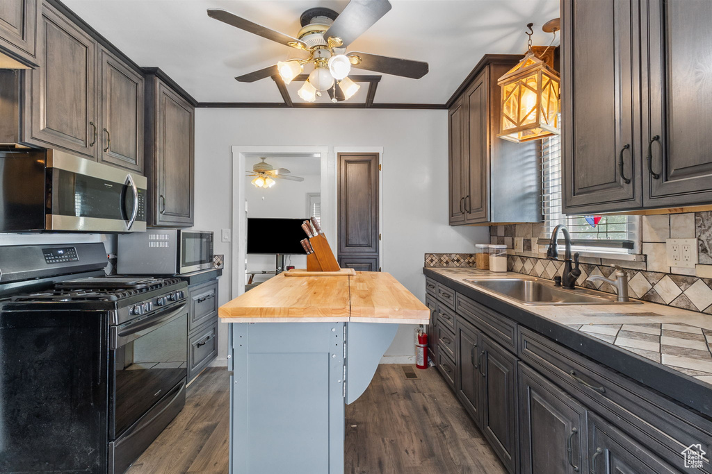 Kitchen with black gas stove, stainless steel microwave, ceiling fan, dark wood-style flooring, and crown molding