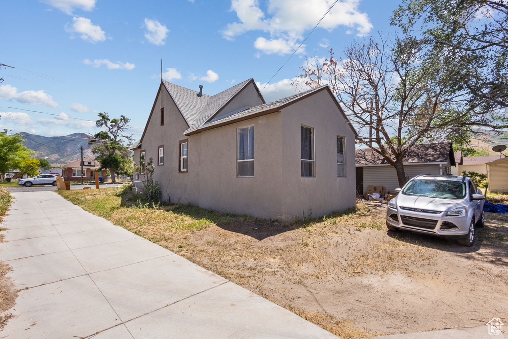 View of property exterior with stucco siding, a mountain view, and a shingled roof