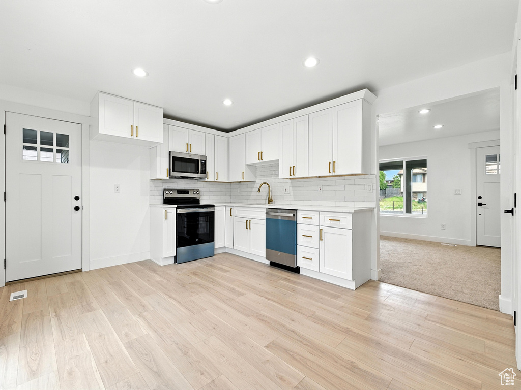 Kitchen with stainless steel appliances, light countertops, backsplash, white cabinetry, and recessed lighting