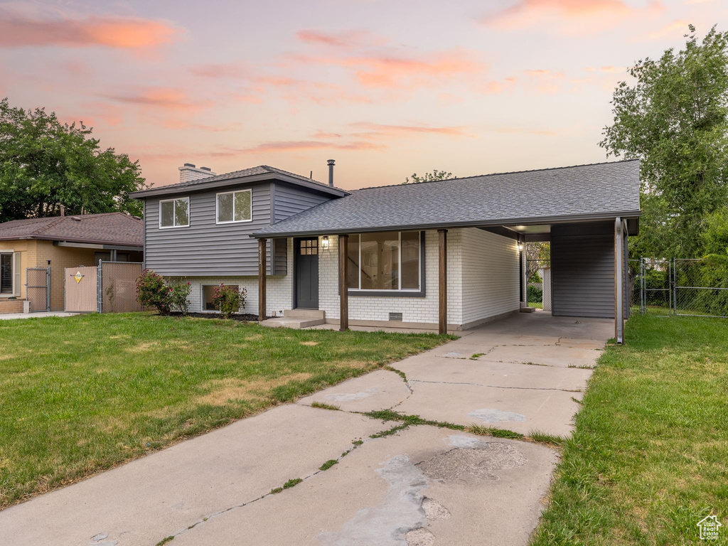 Split level home with a gate, driveway, brick siding, an attached carport, and a chimney