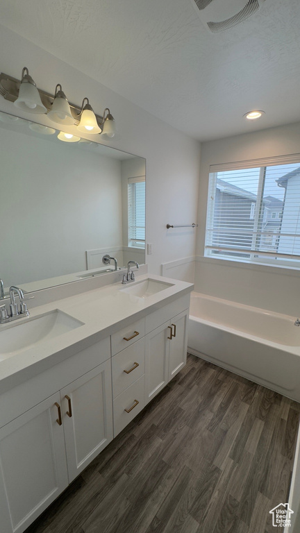 Bathroom with double vanity, wood finished floors, a bath, and recessed lighting