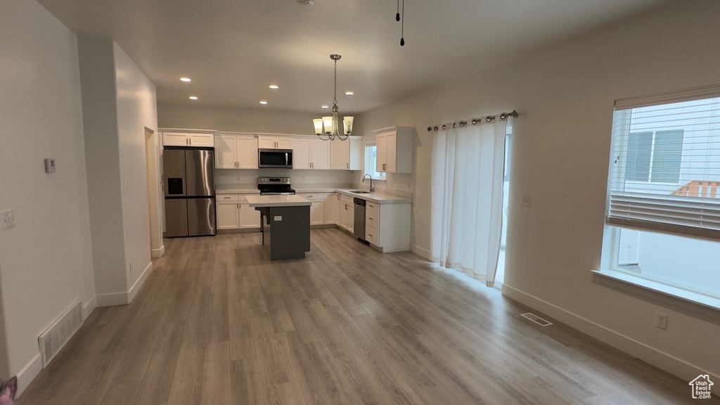 Kitchen featuring stainless steel appliances, a chandelier, light countertops, white cabinets, and light wood-type flooring