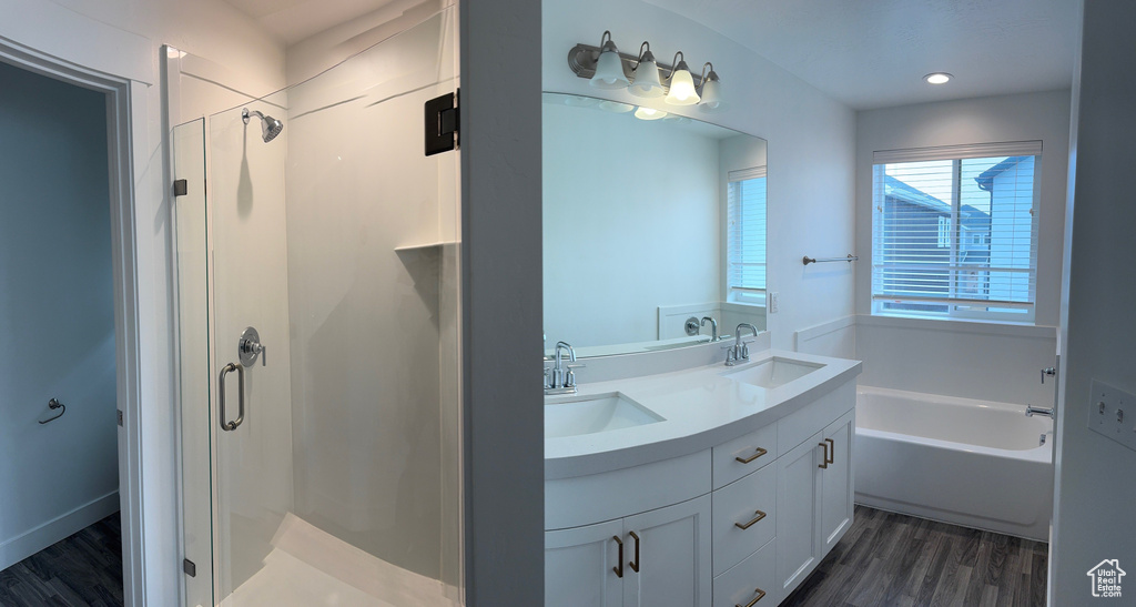 Bathroom with a stall shower, double vanity, wood finished floors, a bath, and recessed lighting