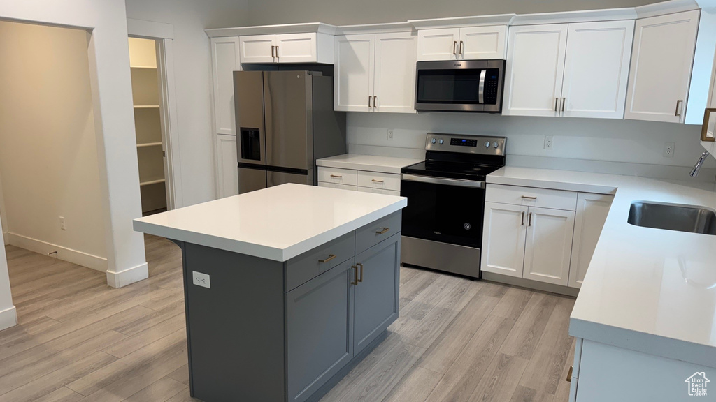 Kitchen featuring stainless steel appliances, light wood finished floors, white cabinetry, and light countertops