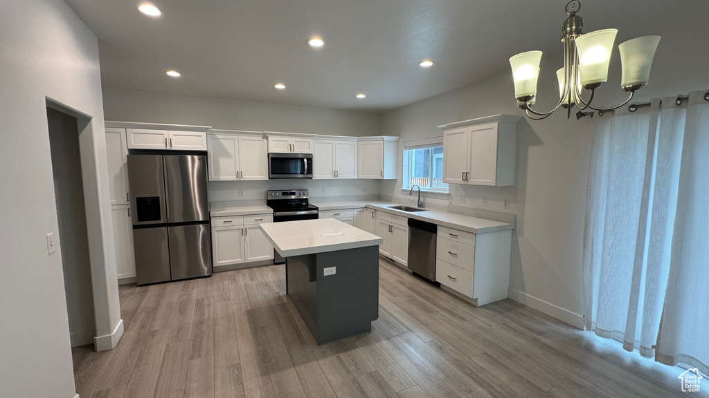 Kitchen with appliances with stainless steel finishes, white cabinetry, light countertops, a chandelier, and light wood-style floors