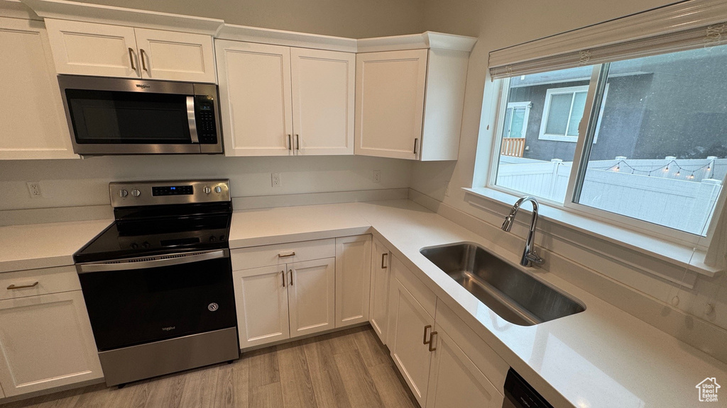 Kitchen with stainless steel appliances, white cabinets, light countertops, and light wood finished floors