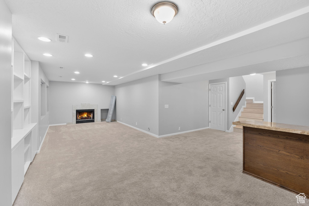 Finished below grade area with light colored carpet, recessed lighting, a fireplace, stairway, and a textured ceiling
