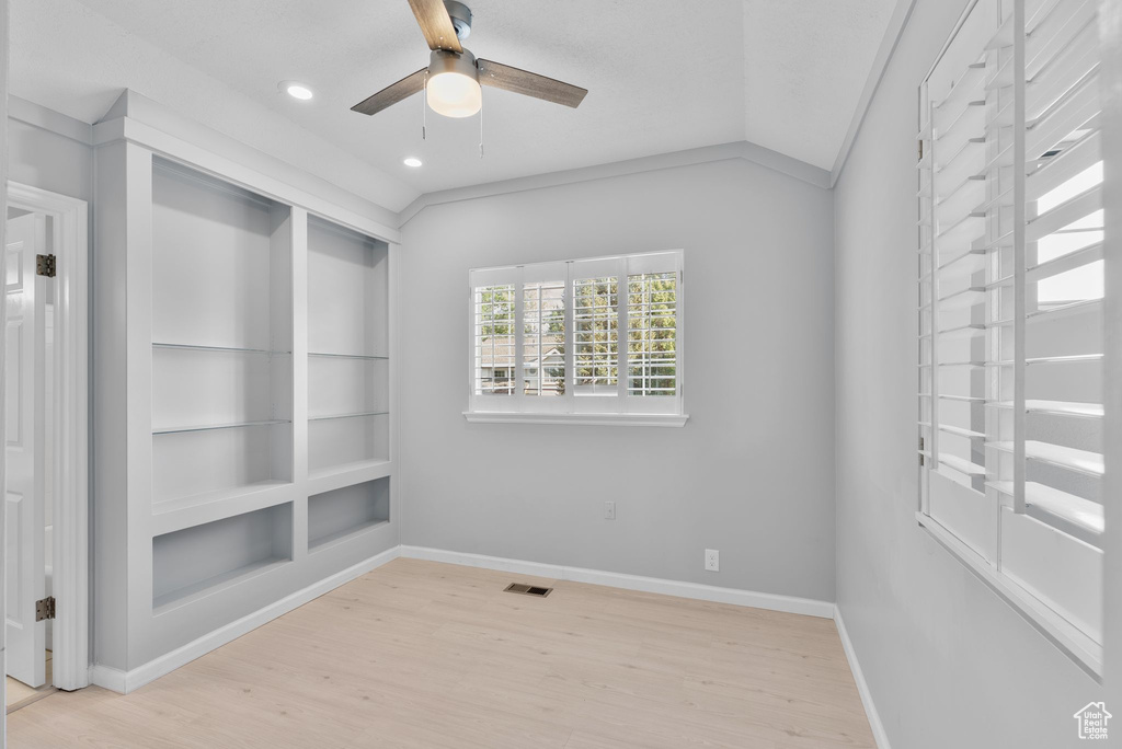 Spare room featuring wood finished floors, ceiling fan, built in shelves, recessed lighting, and vaulted ceiling