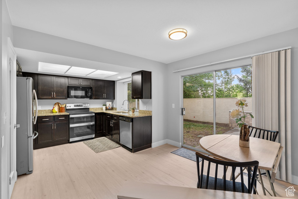 Kitchen with appliances with stainless steel finishes, light wood finished floors, and light stone counters