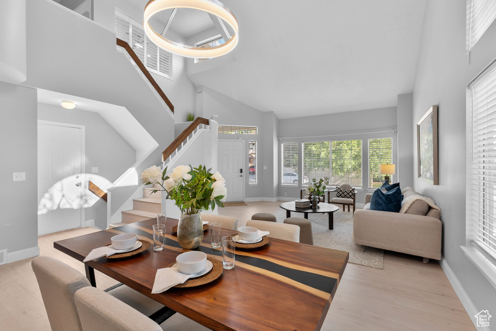 Dining room featuring high vaulted ceiling, stairs, and light wood-style floors