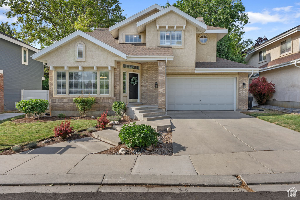 Traditional-style house featuring an attached garage, concrete driveway, brick siding, and stucco siding