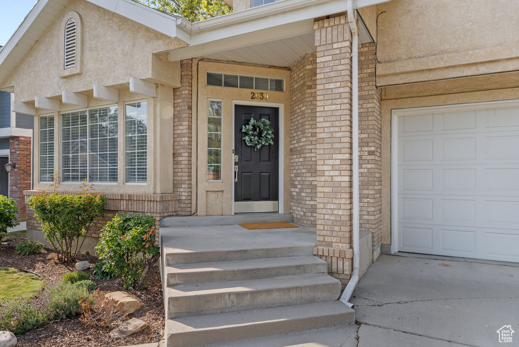 View of exterior entry with brick siding, stucco siding, an attached garage, and driveway