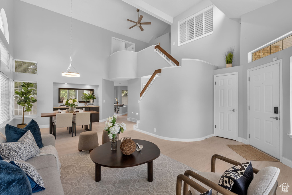 Living room with high vaulted ceiling, light wood-style flooring, beamed ceiling, a ceiling fan, and stairway