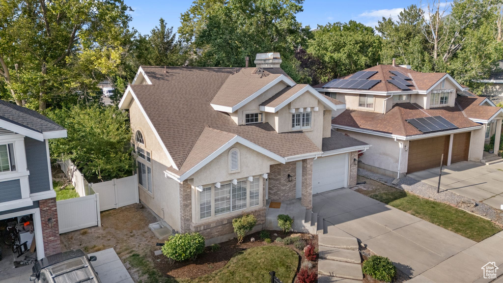View of front of house with concrete driveway, a shingled roof, stucco siding, and view of scattered trees