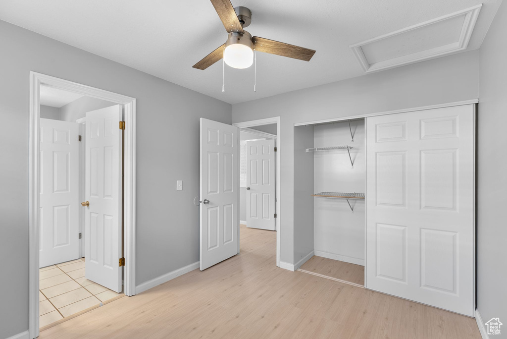 Unfurnished bedroom featuring wood finished floors, attic access, a closet, and ceiling fan