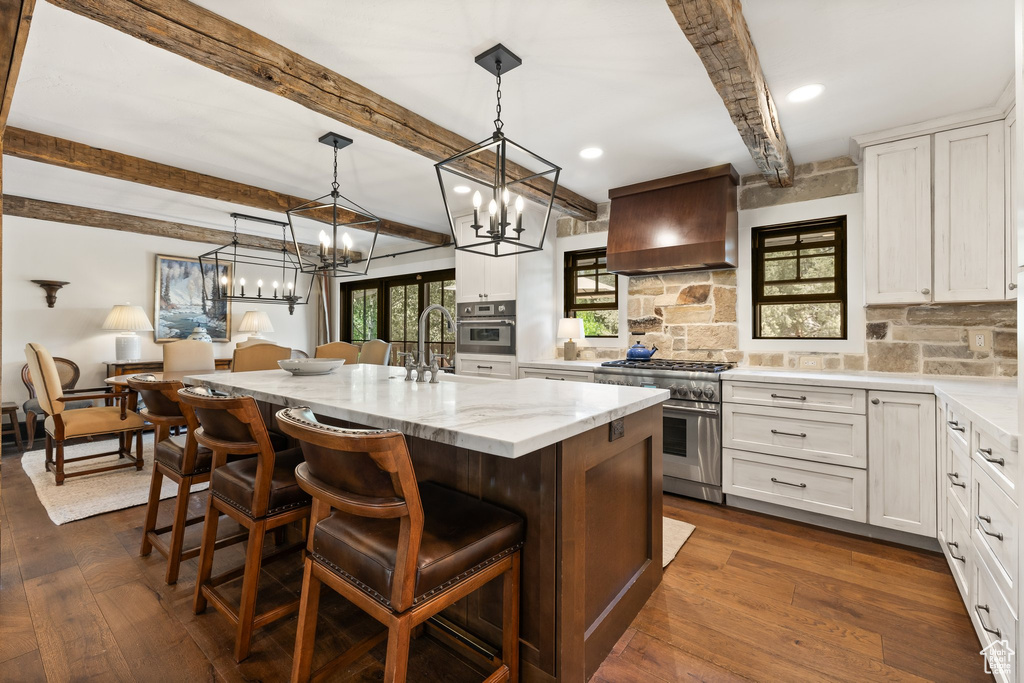 Kitchen with stainless steel appliances, custom exhaust hood, beam ceiling, backsplash, and a center island with sink