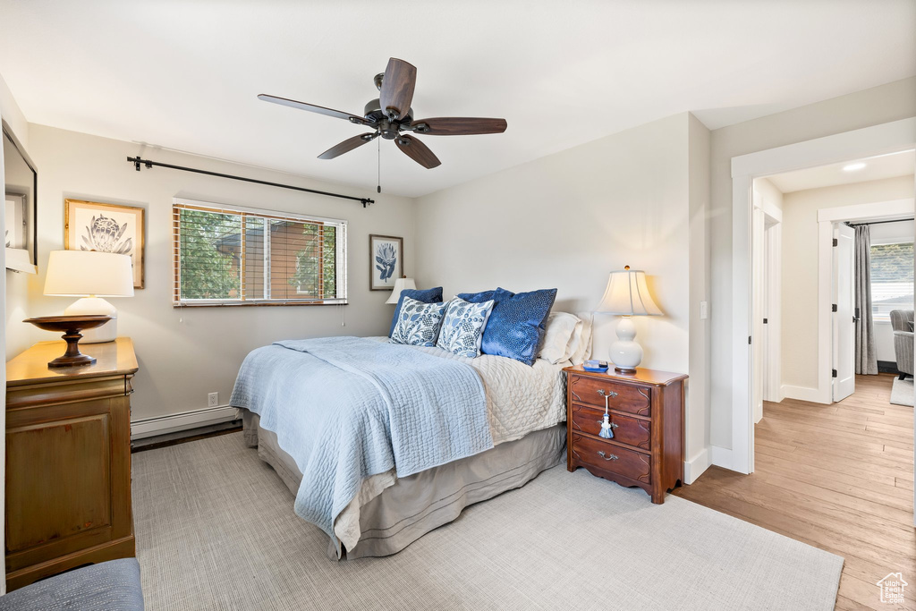 Bedroom with baseboard heating, wood finished floors, and a ceiling fan