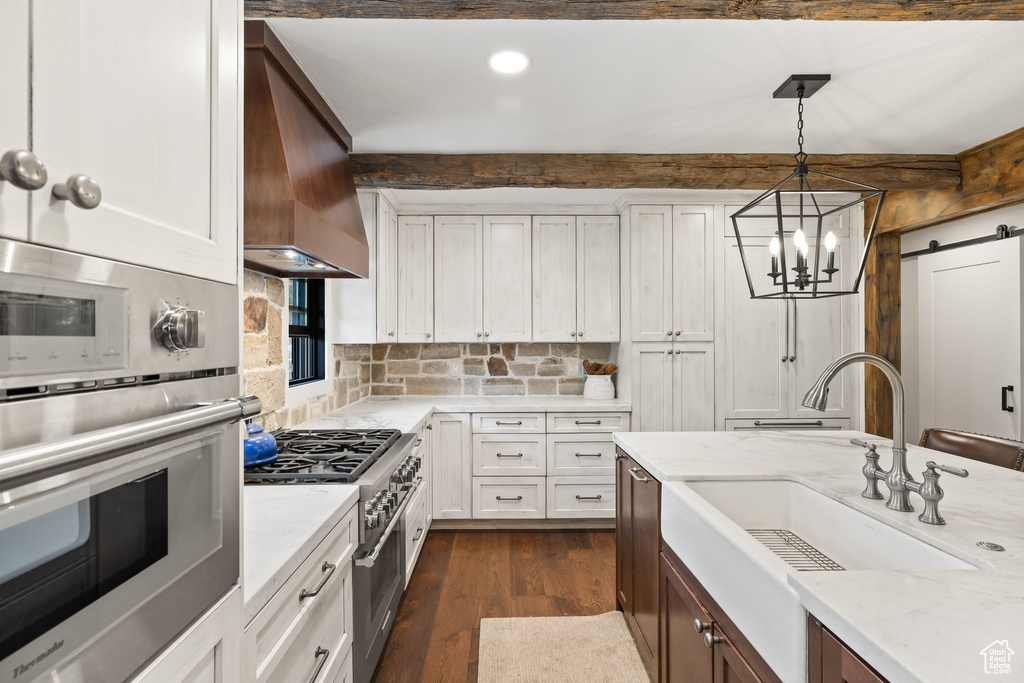 Kitchen featuring stainless steel appliances, custom range hood, a barn door, dark wood-style flooring, and decorative light fixtures