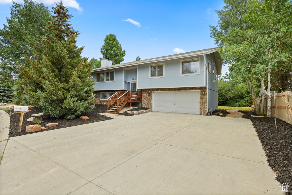 Raised ranch featuring a garage, driveway, a chimney, and stone siding