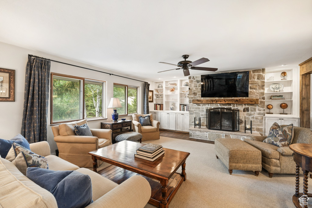 Living area featuring a ceiling fan, built in shelves, a stone fireplace, and wood finished floors