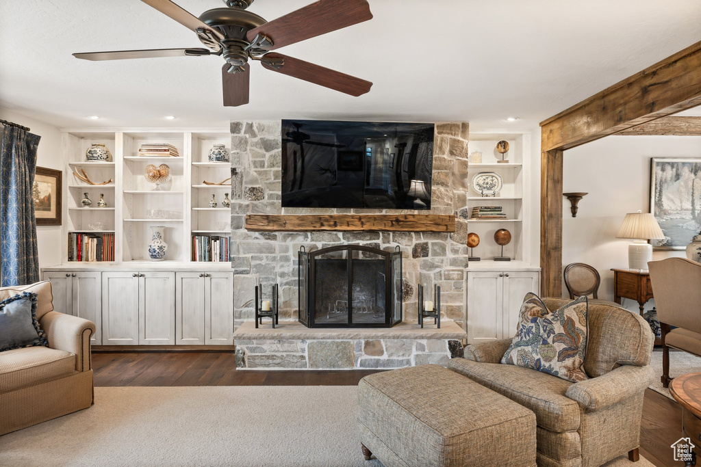 Living room featuring built in features, a ceiling fan, dark wood-style flooring, and a stone fireplace