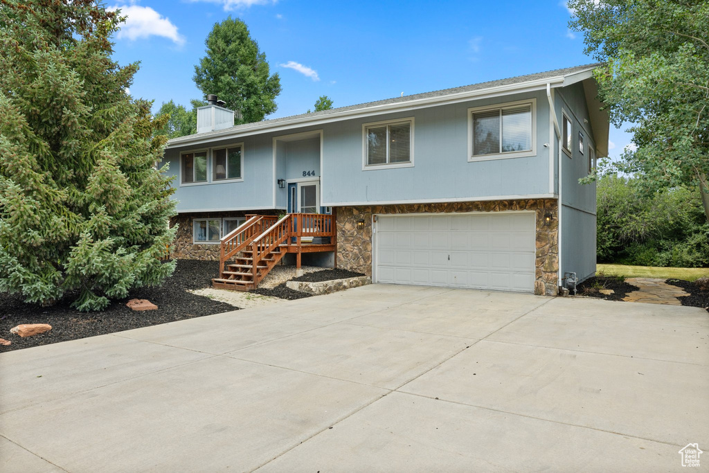 Split foyer home featuring stone siding, a garage, concrete driveway, and a chimney