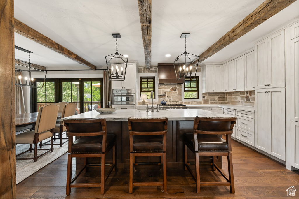Kitchen with a chandelier, stainless steel oven, beamed ceiling, white cabinets, and tasteful backsplash
