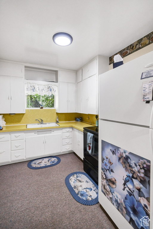 Kitchen featuring freestanding refrigerator, black electric range oven, white cabinets, and dark carpet