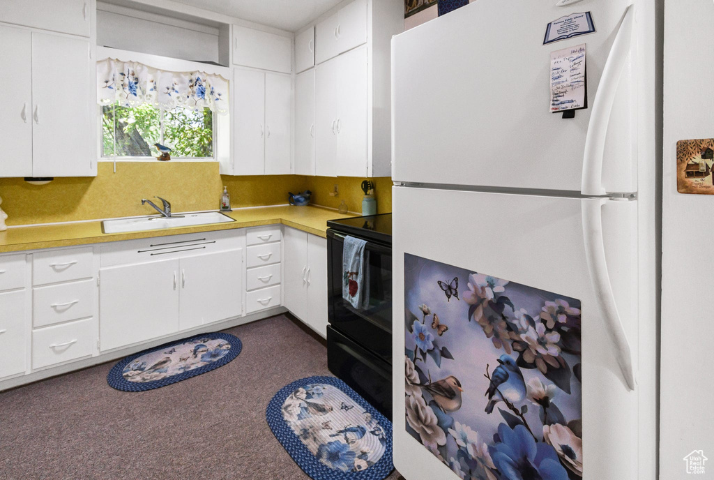 Kitchen with freestanding refrigerator, black / electric stove, light countertops, and white cabinetry