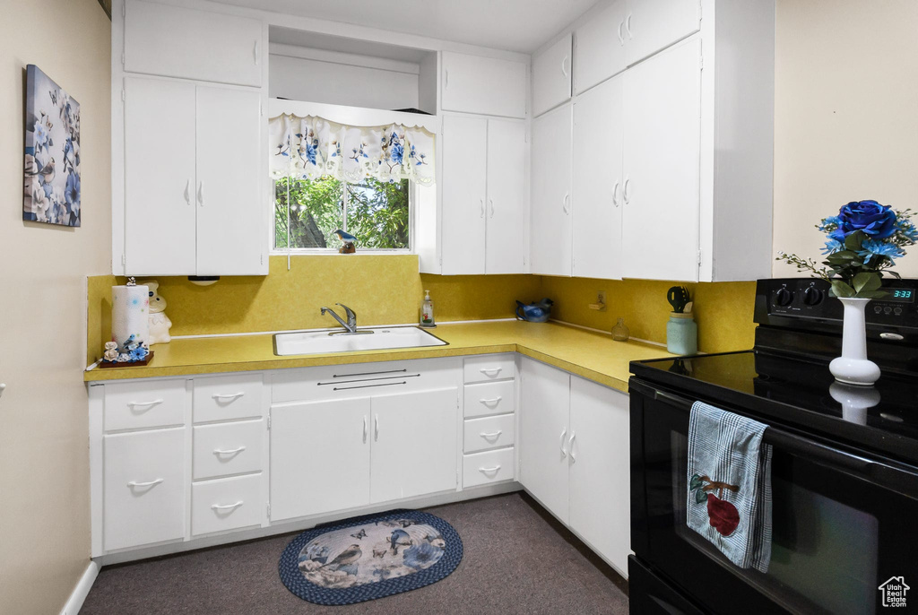 Kitchen featuring black range with electric stovetop, light countertops, white cabinetry, and dark colored carpet