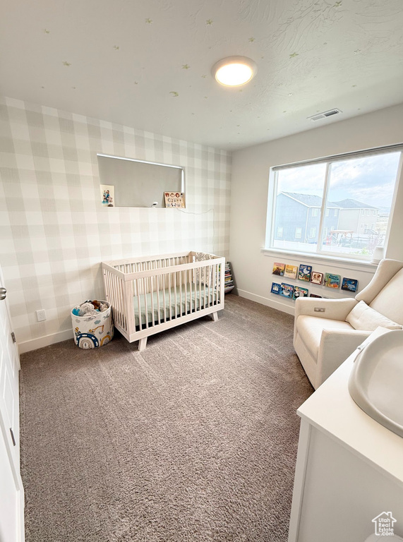 Bedroom featuring wallpapered walls, carpet flooring, and a nursery area