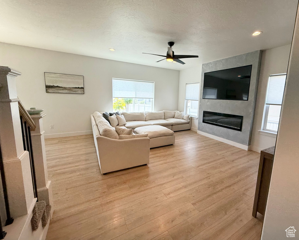 Living room with a fireplace, a ceiling fan, light wood-style flooring, and recessed lighting