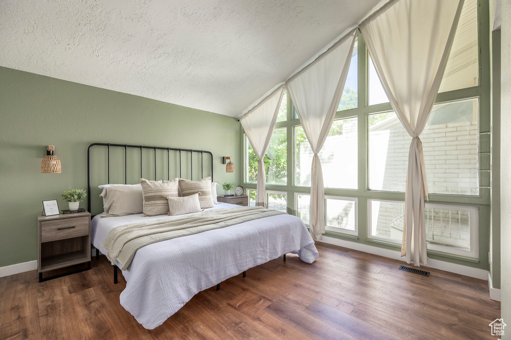 Bedroom with lofted ceiling, a textured ceiling, and wood finished floors