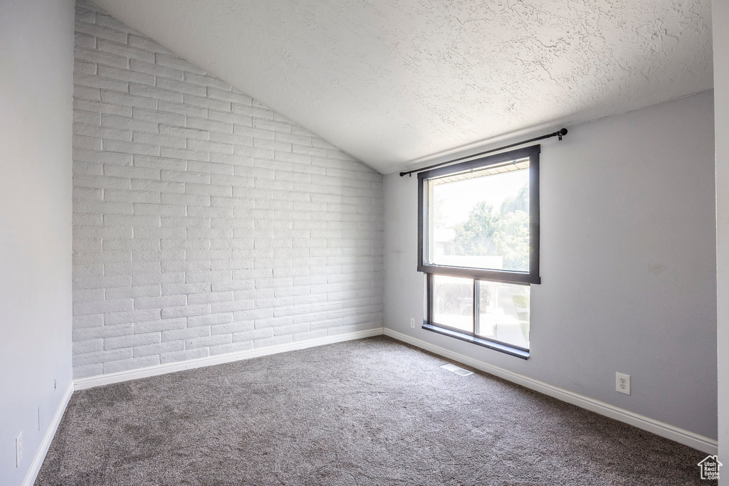 Unfurnished room featuring lofted ceiling, a textured ceiling, carpet flooring, and brick wall