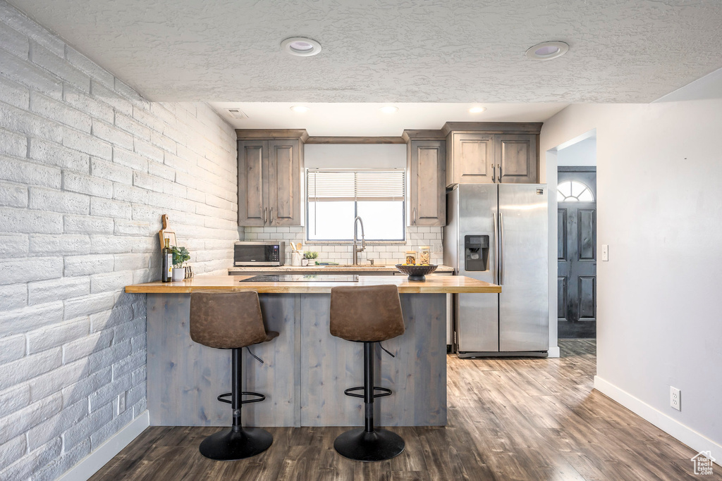 Kitchen featuring appliances with stainless steel finishes, butcher block countertops, a kitchen bar, a peninsula, and a textured ceiling