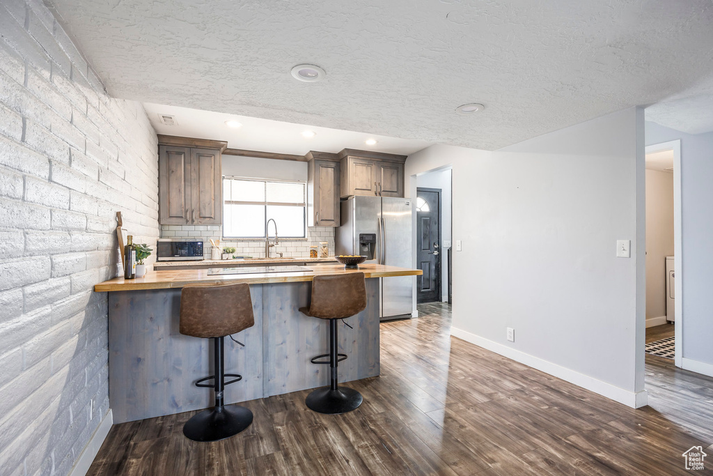 Kitchen with wood counters, appliances with stainless steel finishes, a breakfast bar area, dark wood-type flooring, and a textured ceiling