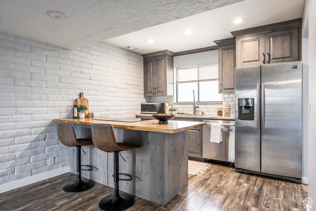 Kitchen with appliances with stainless steel finishes, wood counters, a kitchen breakfast bar, wood finished floors, and backsplash