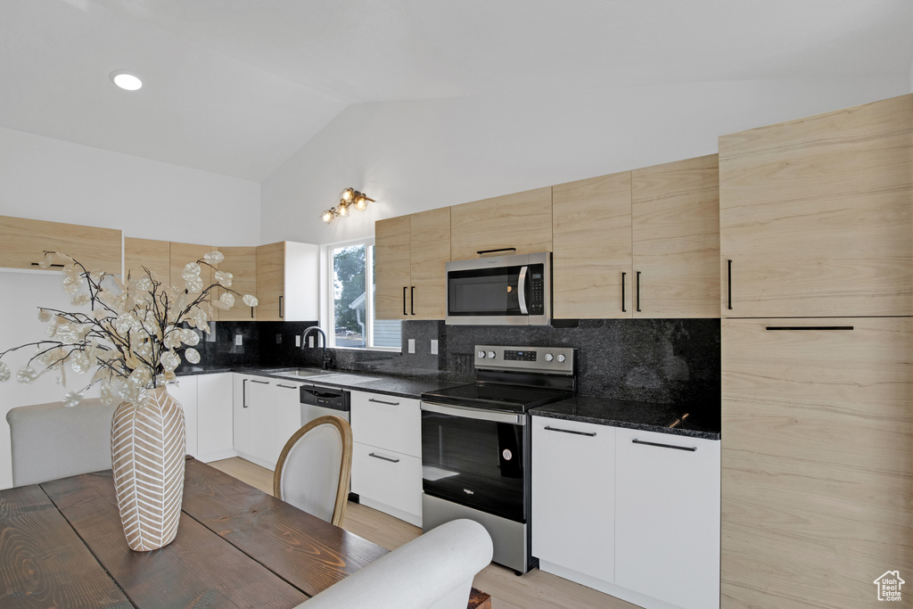 Kitchen with appliances with stainless steel finishes, vaulted ceiling, backsplash, light wood-style floors, and modern cabinets
