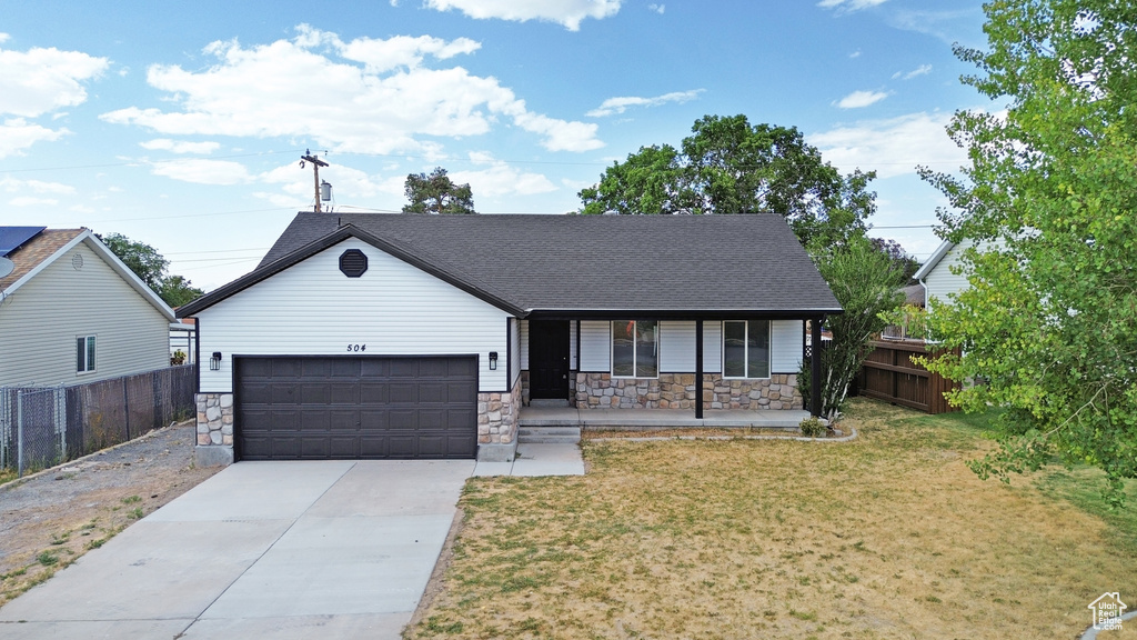 View of front of house with stone siding, a garage, covered porch, and concrete driveway