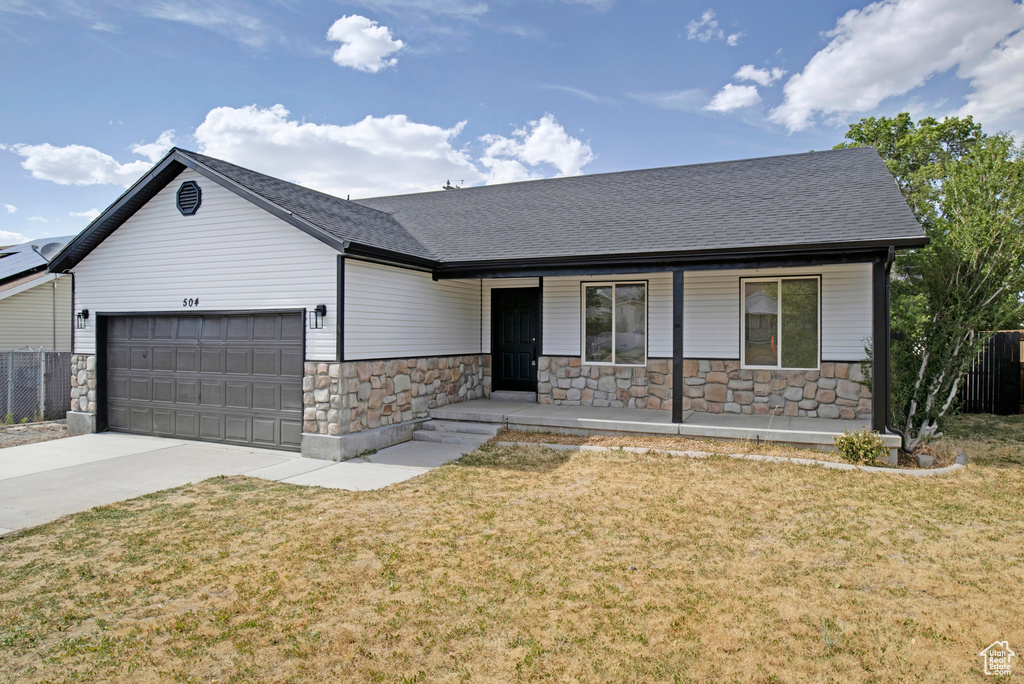 View of front of property with stone siding, covered porch, an attached garage, driveway, and roof with shingles