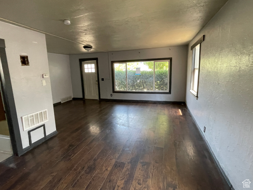 Unfurnished living room featuring dark wood-type flooring and baseboards