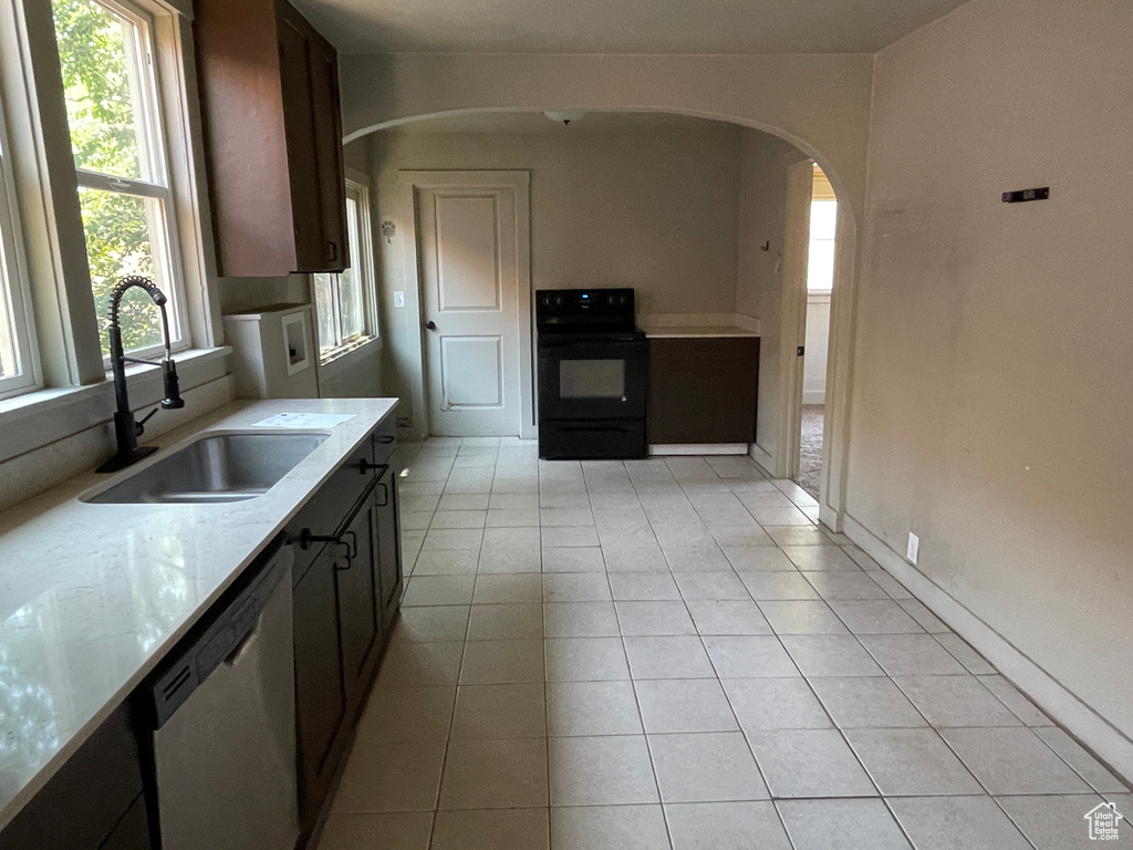 Kitchen featuring black range with electric cooktop, dishwasher, arched walkways, light tile patterned floors, and light stone countertops