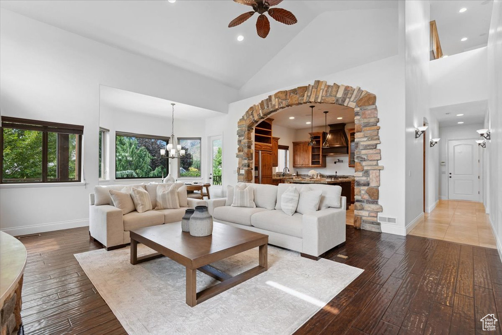 Living area with high vaulted ceiling, ceiling fan, wood-type flooring, a chandelier, and arched walkways