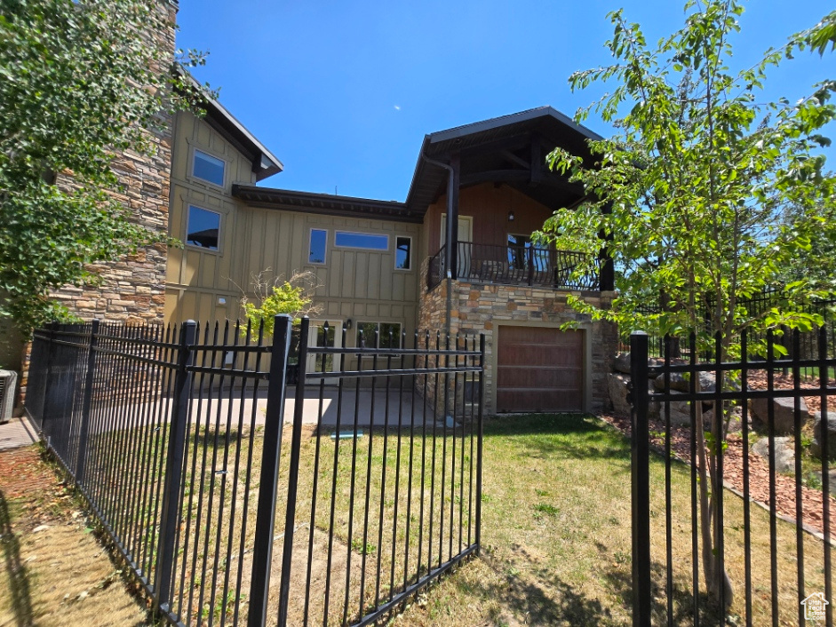 View of front of house featuring a fenced front yard, stone siding, a balcony, and a garage
